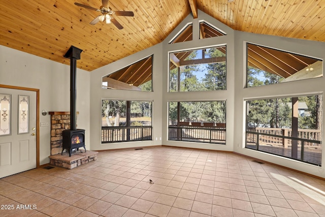 unfurnished sunroom with ceiling fan, a wood stove, wood ceiling, and vaulted ceiling with beams