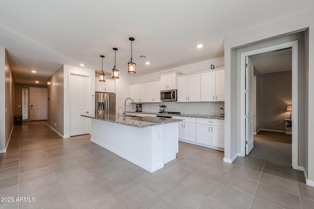 kitchen featuring stainless steel appliances, dark stone countertops, white cabinetry, and an island with sink