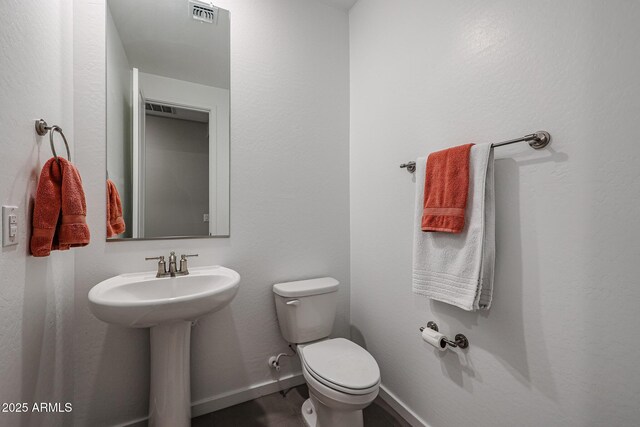 half bath with visible vents, a sink, toilet, and baseboards