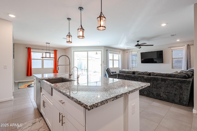 kitchen with light stone counters, white cabinets, hanging light fixtures, and an island with sink