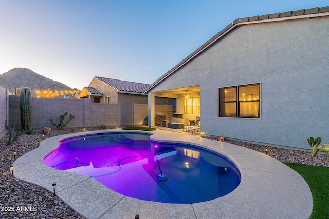 pool at dusk featuring a fenced backyard, a mountain view, a fenced in pool, and a patio