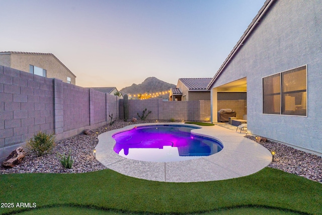 pool at dusk with a patio area, a fenced backyard, and a fenced in pool