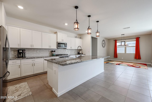 kitchen featuring stainless steel appliances, hanging light fixtures, an island with sink, and white cabinetry