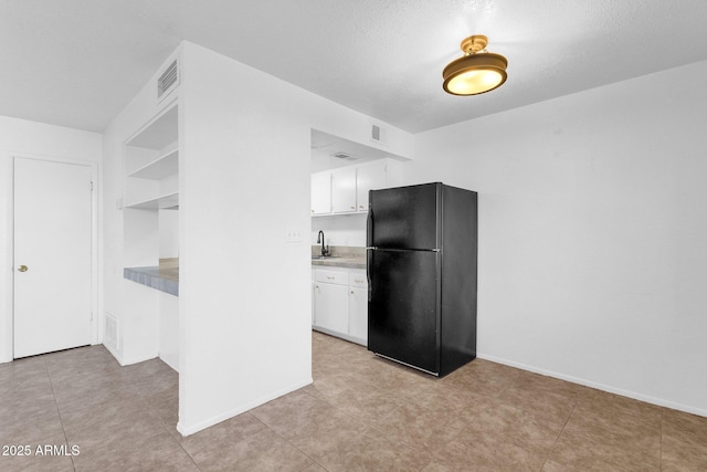 kitchen with white cabinetry, black refrigerator, sink, and a textured ceiling