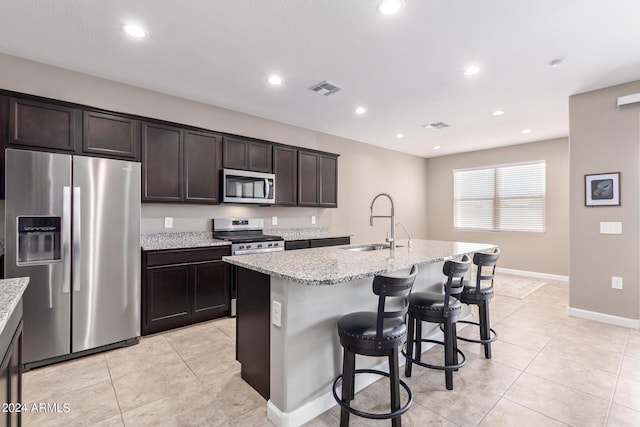 kitchen with a kitchen island with sink, light stone countertops, sink, and stainless steel appliances