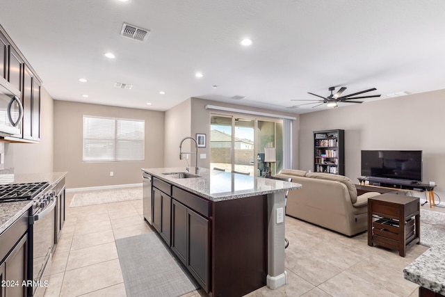 kitchen with ceiling fan, sink, appliances with stainless steel finishes, dark brown cabinets, and light stone counters