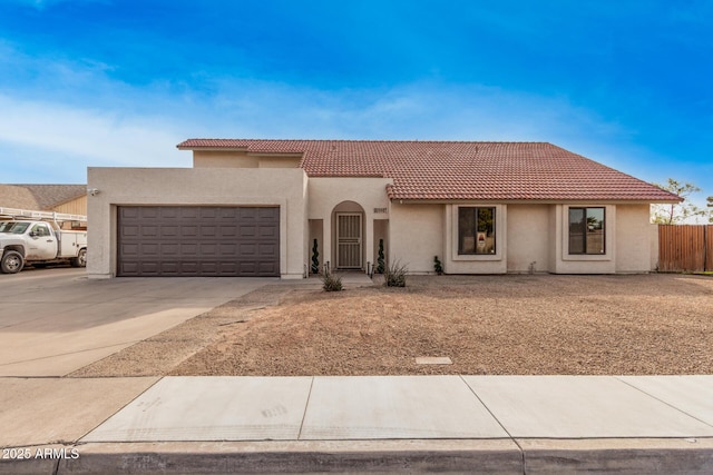 mediterranean / spanish house with a garage, driveway, a tiled roof, fence, and stucco siding