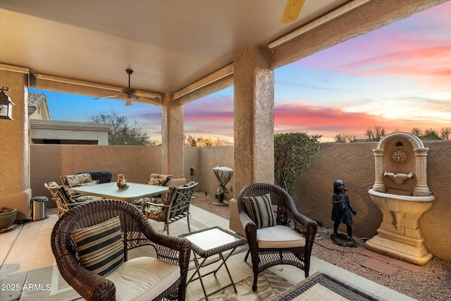 patio terrace at dusk with a ceiling fan, outdoor dining space, and a fenced backyard