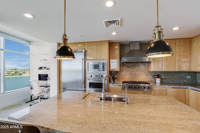 kitchen with a water view, wall chimney range hood, sink, light stone countertops, and stainless steel appliances