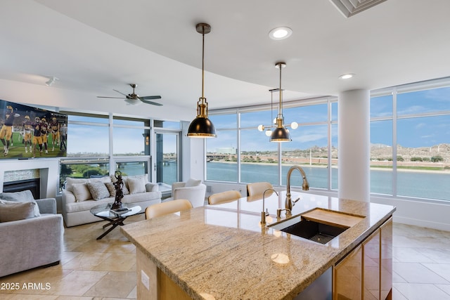 kitchen with light stone counters, ceiling fan, sink, a water view, and a center island with sink