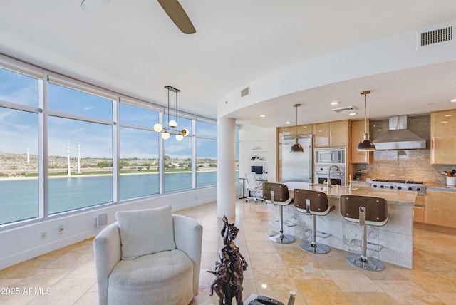 kitchen with a water view, built in appliances, wall chimney exhaust hood, decorative backsplash, and decorative light fixtures