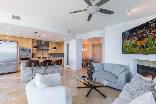 living room with a fireplace, sink, light tile patterned floors, and ceiling fan with notable chandelier