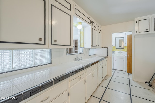1945 E Solano Dr, Phoenix, AZ 85016 - kitchen with tile countertops, tasteful backsplash, white cabinetry, light tile patterned flooring, and washer / dryer