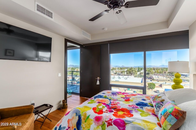 bedroom featuring ceiling fan, access to exterior, hardwood / wood-style floors, and a tray ceiling