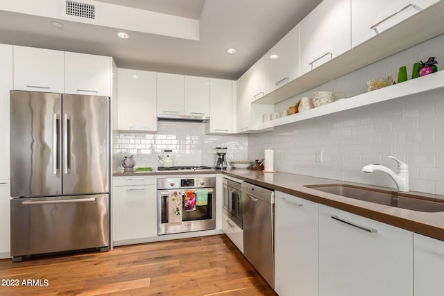 kitchen with appliances with stainless steel finishes, sink, backsplash, white cabinetry, and light hardwood / wood-style floors