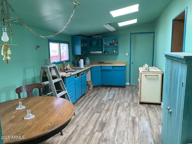 kitchen featuring light hardwood / wood-style floors, blue cabinets, vaulted ceiling, and sink