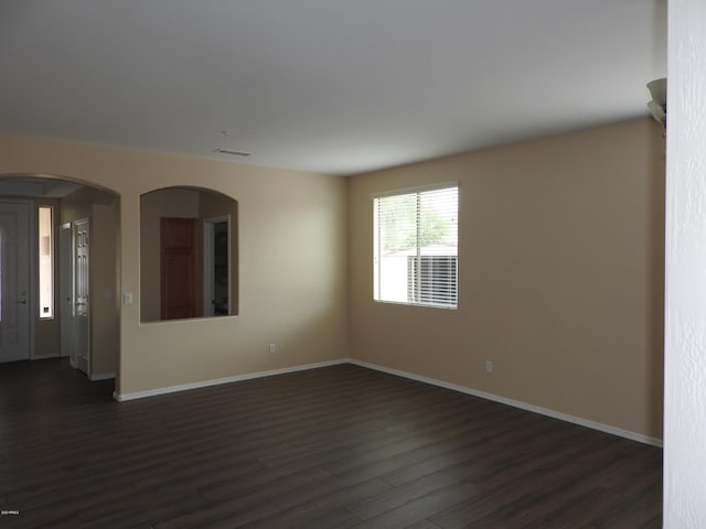 spare room featuring dark wood-style floors, arched walkways, and baseboards