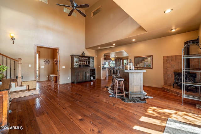 living room featuring ceiling fan, dark hardwood / wood-style floors, bar area, a towering ceiling, and a wood stove