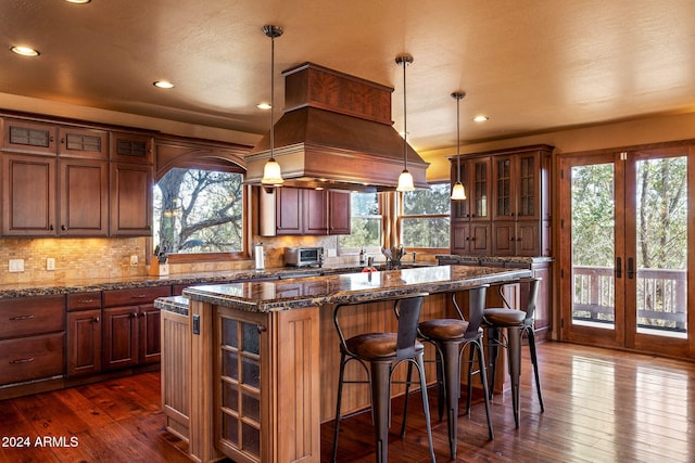 kitchen featuring tasteful backsplash, a kitchen island, dark stone counters, dark hardwood / wood-style floors, and decorative light fixtures