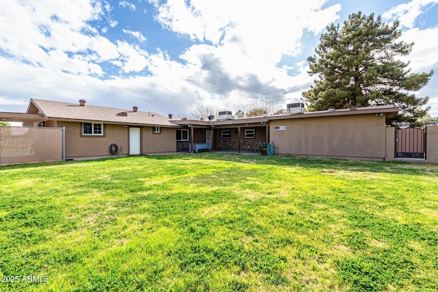 back of house featuring stucco siding, a lawn, and fence