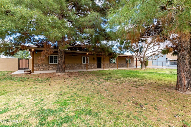 exterior space with a gate, stone siding, a patio, fence, and a yard