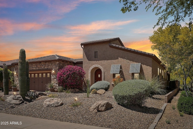 mediterranean / spanish-style house featuring a garage, stucco siding, stone siding, and a tile roof