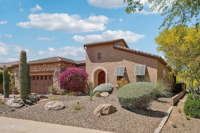 mediterranean / spanish-style home with a garage, a tiled roof, stucco siding, and stone siding