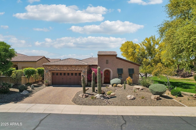 mediterranean / spanish-style home with a tiled roof, stone siding, a garage, stucco siding, and decorative driveway