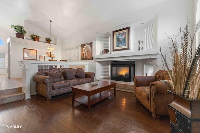 living room featuring an inviting chandelier, lofted ceiling, wood finished floors, and a lit fireplace