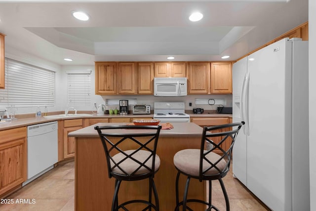 kitchen with a kitchen island, a breakfast bar area, recessed lighting, white appliances, and a raised ceiling