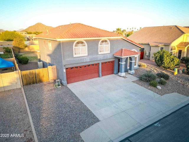 mediterranean / spanish house with stucco siding, driveway, a tile roof, fence, and an attached garage