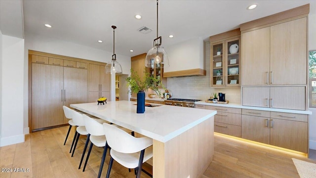 kitchen with custom exhaust hood, light brown cabinets, decorative light fixtures, light wood-type flooring, and a large island