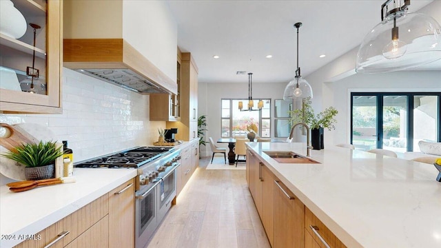 kitchen with light wood-type flooring, high end stainless steel range oven, sink, exhaust hood, and hanging light fixtures