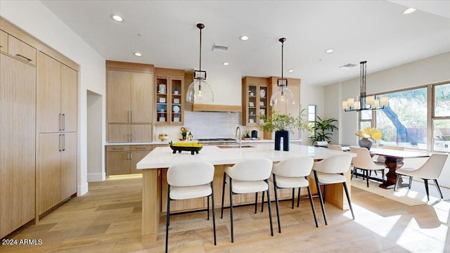 kitchen featuring a large island with sink, an inviting chandelier, hanging light fixtures, decorative backsplash, and light wood-type flooring