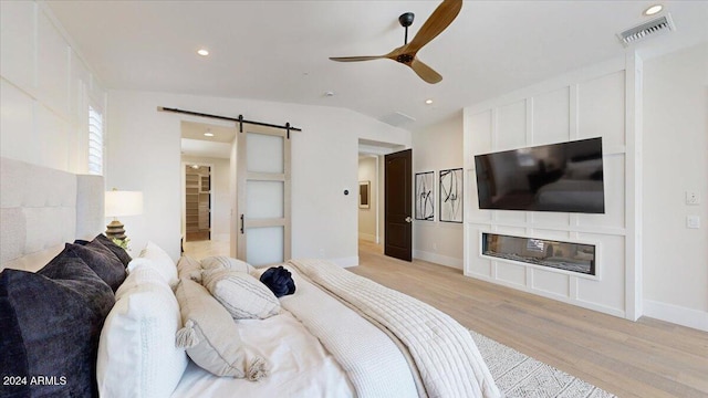 bedroom with ceiling fan, a barn door, light wood-type flooring, and lofted ceiling