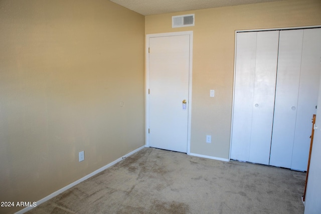 unfurnished bedroom with a textured ceiling, light colored carpet, and a closet