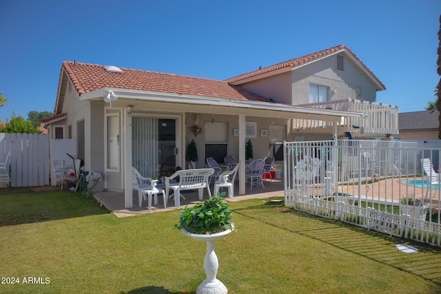 rear view of property with a lawn, a patio area, a fenced in pool, and a balcony