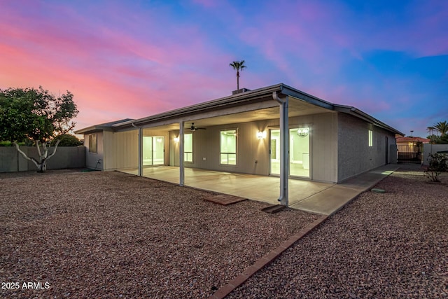 back house at dusk with ceiling fan and a patio