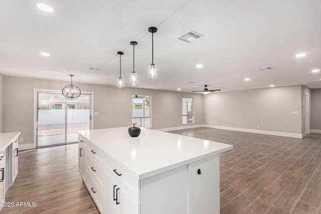 kitchen featuring white cabinets, decorative light fixtures, a kitchen island, and ceiling fan with notable chandelier