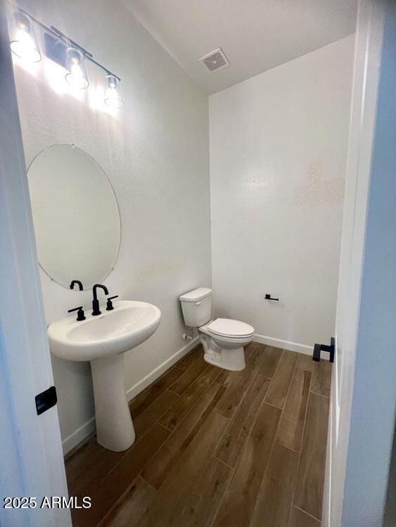 half bath featuring visible vents, toilet, baseboards, and wood tiled floor