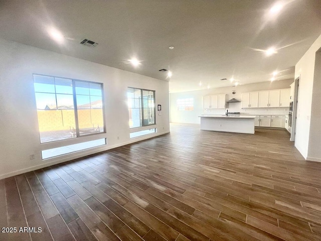 unfurnished living room with dark wood finished floors, a healthy amount of sunlight, visible vents, and baseboards