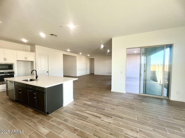 kitchen with wood finish floors, a sink, open floor plan, appliances with stainless steel finishes, and light countertops