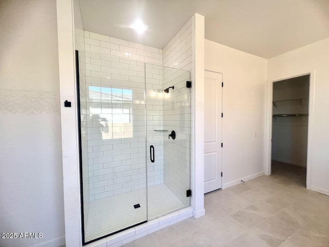 bathroom featuring a walk in closet, baseboards, and a stall shower