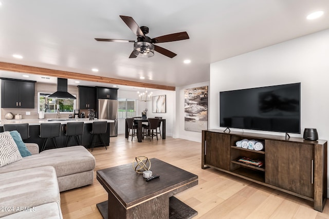 living room with ceiling fan with notable chandelier, sink, light wood-type flooring, and a healthy amount of sunlight