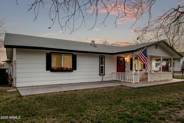 back of house at dusk featuring a porch, a lawn, a shingled roof, and central air condition unit