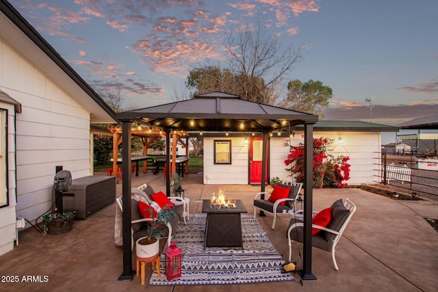 patio terrace at dusk featuring an outdoor living space with a fire pit, fence, grilling area, and a gazebo