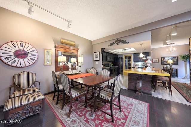 dining area featuring rail lighting, wood finished floors, a textured ceiling, and a chandelier