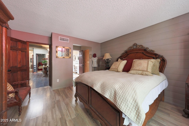 bedroom with light wood-style floors, a textured ceiling, and wood walls