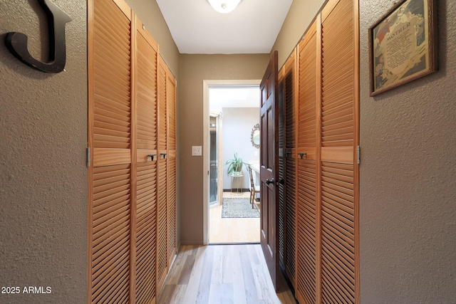 hallway with light wood-type flooring and a textured wall
