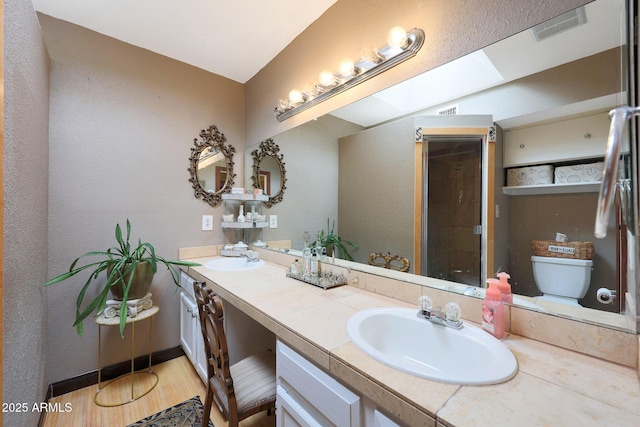 full bath featuring a skylight, tiled shower, wood finished floors, double vanity, and toilet